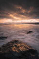 A stunning sunset over a rocky beach with waves gently crashing against the shoreline and colorful skies in a dramatic seascape