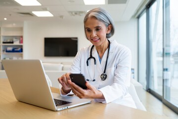 Senior Female Doctor Checking Smartphone at Desk
