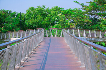 Greenbelt - PIK 2, June 26, 2025 : a curved pedestrian footbridge in Jakarta, Banten, Indonesia, constructed of concrete with a wood-look flooring, set within a park landscape.
