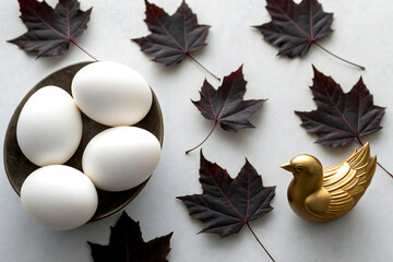 Minimalistic Close-Up of White Eggs and Gold Bird Sculpture on Fall Leaves
