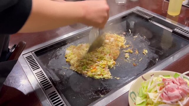 cooking monja yaki. tokyo local food. a chorus of blades on a sizzling iron pan stage.