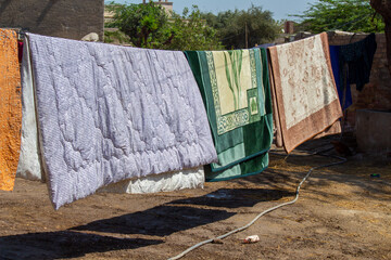 Colorful quilts and blankets hanging on a rope clothesline under the sun in a rural household. A common drying method in South Asia.

