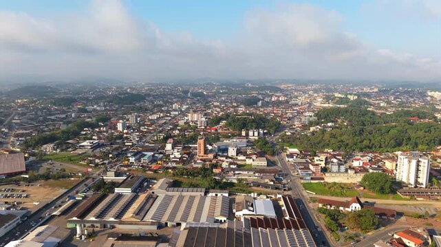 Drone pivots from urban sprawl to more vegetated slopes, where trees and clouds soften Joinville&rsquo;s edges. Ideal for ecological contrast or regional serenity.
