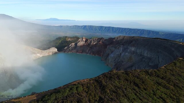 Right-orbit aerial glides over Kawah Ijen at dawn, revealing its turquoise acidic crater lake, sulfur steam plumes and jagged caldera walls set against mist-shrouded East Javan ranges.