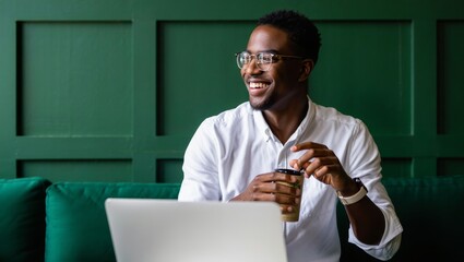 Happy african american man working on laptop with coffee in modern green office