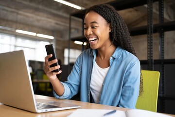 Happy african american woman using smartphone and laptop for video call at desk office