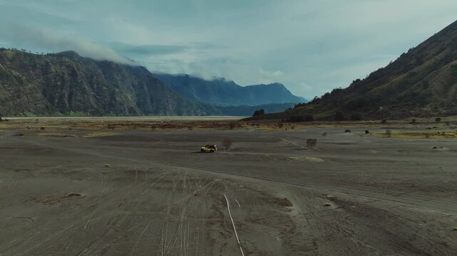 Yellow vehicle traverses the vast "Sea of Sand," a volcanic plain at the foot of the rugged Mount Batok in the Bromo caldera.