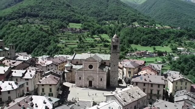 Stone Church and Terracotta Roofs in Quaint Italian Village Aerial View Amidst Rolling Green Mountains Under Bright Sky