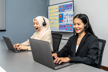 Two female customer service representatives wearing headsets working on laptops in office call...