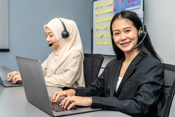 Two female customer service representatives wearing headsets working on laptops in office call...