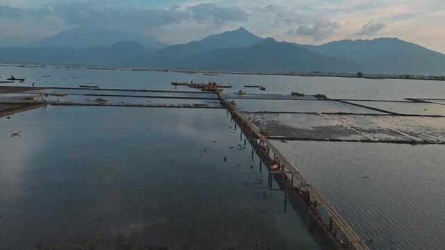 Sweeping Aerial View of a Serene Lake Bamboo Bridge and Majestic Mountains at Sunrise.