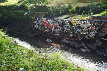 Massive Plastic Pollution: Accumulation of Waste Clogging a Murky Drainage Ditch, Highlighting...