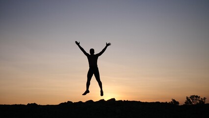 Silhouette of Freedom: A silhouette of a person, leaping into the air against the backdrop of a...
