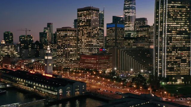 Night view of San Francisco's illuminated skyline and the Ferry Building. Cars move along the Embarcadero in the USA. Cityscape photography.