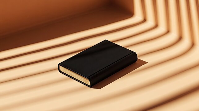 A black hardcover book with gold gilded edges rests on a pale orange surface, angled subtly, illuminated by dramatic, striped sunlight - Powered by Adobe