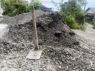 A pile of gravel with a shovel resting on top in a natural setting.