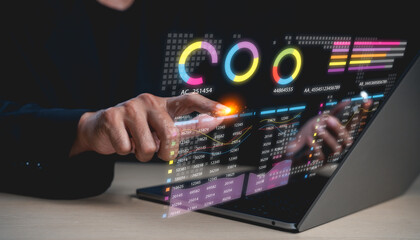 A person interacts with a futuristic transparent touchscreen displaying colorful charts and data...