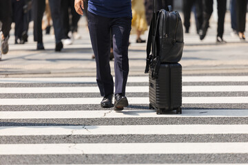 スーツケースを押して横断歩道を渡るビジネスマンの足元