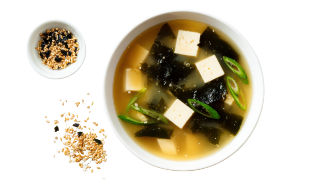 Miso soup with tofu and seaweed, garnished with green onions and sesame seeds, isolated on a white background.