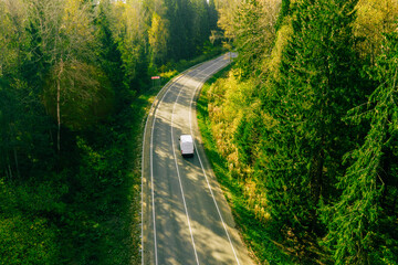 Aerial drone view of cars driving asphalt road through summer or fall woods