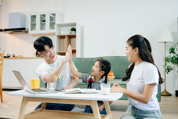 Asian parents cheering and guiding daughter through homework at home. Joyful teamwork, love, and learning in a cozy,