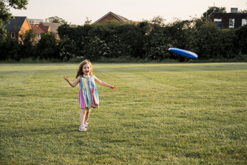 Little girl playing frisbee in the park at sunset