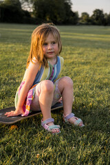 Little girl playing sitting on a skateboard in the park, sunset
