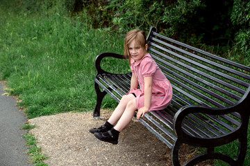 Little girl sitting on a bench in the park in school uniform dress