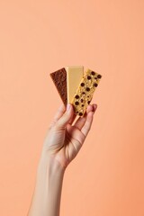 A hand holds three types of chocolate bars against a soft orange background.