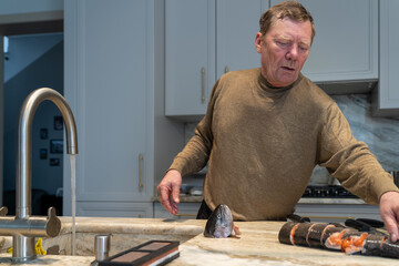 A mature man meticulously preparing fresh salmon or trout in a contemporary home kitchen, with cut...