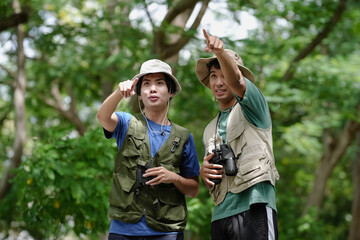 Bird watching is recreational pursuit. Young man and friend have fun with outdoors leisure activity looking up for bird in nature public park. Gay couple enjoy using binocular for bird watch adventure