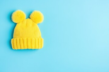 Bright yellow knitted beanie with large pom-poms on a light blue background