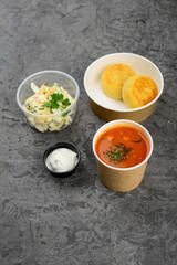 lunch borscht, two cutlets with coleslaw in disposable dishes on a gray background