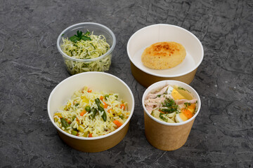 lunch soup, rice with vegetables and cutlet with coleslaw in disposable dishes on a gray background