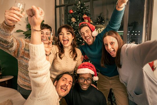 Group of diverse friends taking a selfie at a fun Christmas party. A multi-ethnic group of young people shouting with joy and celebrating the holidays or New Year's Eve together. - Powered by Adobe