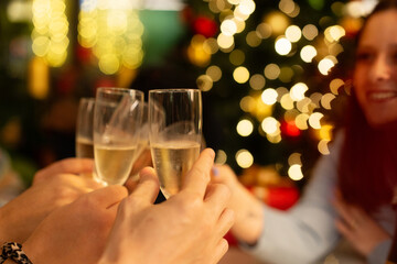 Friends toasting with champagne with Christmas lights bokeh in background. A group celebrates the holidays with a festive cheer, holding glasses of sparkling wine at a party.