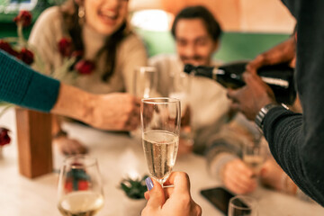 Point of view of getting a glass of champagne poured at a holiday party. First-person perspective of a toast and celebration with friends at a festive New Year's Eve dinner.