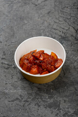 fried meat in tomato sauce in a disposable dish on a gray background