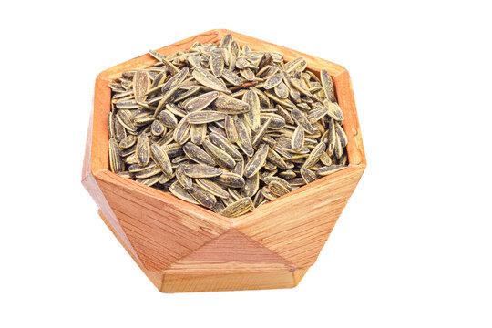 A wooden hexagonal bowl filled with roasted sunflower seeds in their shells, captured from a top-down angle on a white background. The seeds are tightly packed and roasted to a light