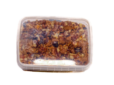 A rectangular plastic container filled with mixed traditional nuts, raisins, dried figs, and possibly pieces of rock candy. The medley has a rich, rustic appearance with various shades of brown, beige