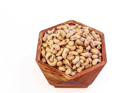 A natural wooden bowl in a hexagon shape brimming with lightly roasted cashew nuts. The image features clean lighting and a white background that emphasizes the earthy color and curved