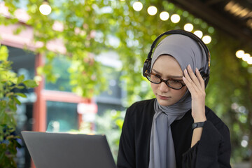 muslim women wear hijab sitting at work using a laptop and headache. Migraines, dizziness from work, lack of sleep.