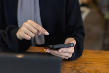 Close-up mobile phone in female hand use searching data networks or chatting online. typing sending message. Muslim women in hijab using smartphone at home blur background.