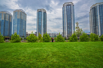 Modern high-rise residential buildings stand tall behind a vibrant green lawn and lush trees under...