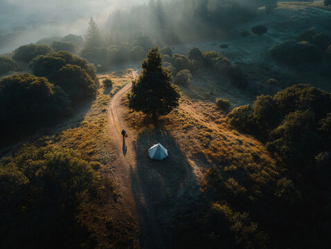 Lone camper walks past tent at sunrise in golden forest hills