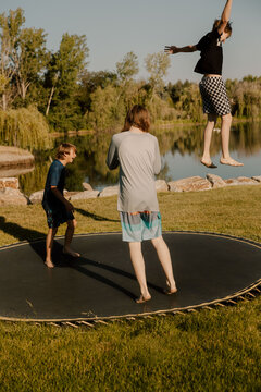 Boys jumping on trampoline by lake in summer