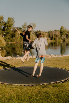 Three kids jumping together on trampoline by a calm lake