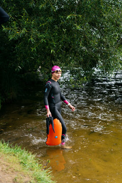 Woman in a wetsuit and a buoy enters the water on lake