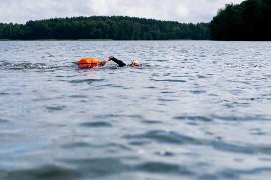 Woman in wetsuit with buoy swimming across lake, open water training
