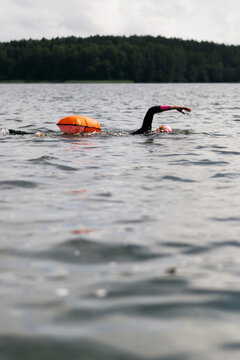 Woman in wetsuit with buoy swimming across lake, open water training